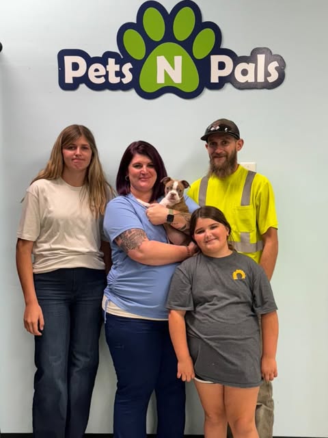 Family holding a puppy beneath the Pets N Pals store sign
